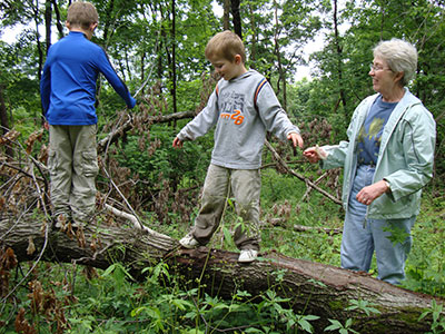 Two kids balancing on log with woman looking on